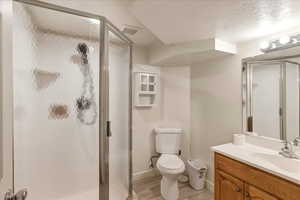 Full bath featuring vanity, a textured ceiling, a stall shower, and light wood finished floors