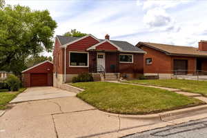 View of front of house with a chimney, a front lawn, an outdoor structure, brick siding, and a garage