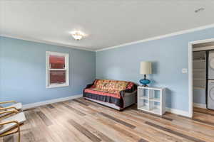 Living area with stacked washer and clothes dryer, crown molding, and light wood finished floors