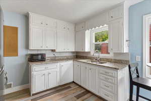 Kitchen with light stone countertops, white cabinetry, light wood-type flooring, and black microwave