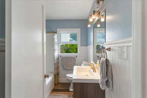 Bathroom featuring vanity, a wainscoted wall, light wood finished floors, and shower / bath combo