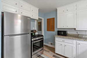 Kitchen with stainless steel appliances, white cabinets, and light wood-style flooring