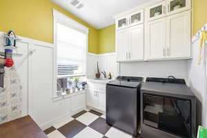 Laundry area featuring a decorative wall, wainscoting, washer and dryer, dark floors, and cabinet space