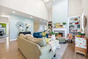 Living room featuring a tile fireplace, built in features, a high ceiling, and wood finished floors