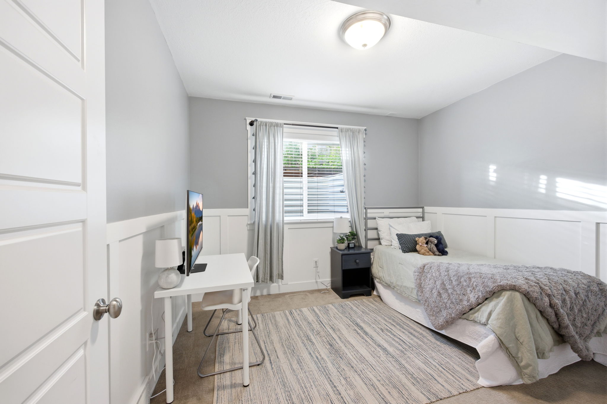 Bedroom featuring wainscoting, a decorative wall, a desk, and light colored carpet