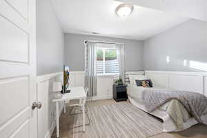 Bedroom featuring wainscoting, a decorative wall, a desk, and light colored carpet