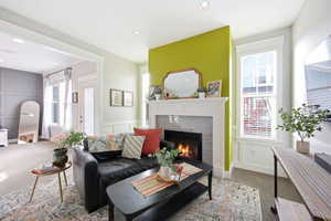 Living area with carpet floors, a tiled fireplace, recessed lighting, and a decorative wall