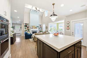Kitchen with a fireplace, a center island, light stone counters, dark wood finish cabinetry, and double oven