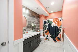 Full bathroom featuring vanity, wainscoting, a shower with shower curtain, and light tile patterned floors