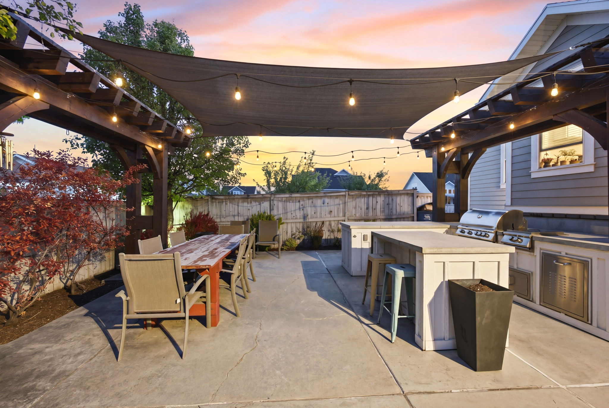 Patio terrace at dusk with an outdoor bar and dining area, exterior kitchen, a pergola, a patio, and a fenced backyard