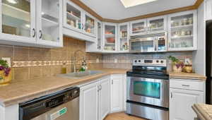 Kitchen with stainless steel appliances, white cabinets, decorative backsplash, glass insert cabinets, and tile counters