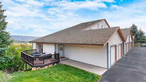 Back of property with stucco siding, a wooden deck, a shingled roof, and a lawn