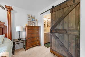 Bedroom with a barn door, light colored carpet, and ensuite bathroom