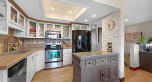 Kitchen featuring stainless steel appliances, light wood-style floors, a kitchen island, two tone color scheme, and glass insert cabinets