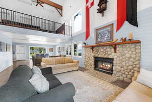 Living area featuring wood walls, a fireplace, ceiling fan, wood finished floors, and a high ceiling