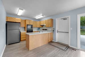 Kitchen featuring tile counters, a peninsula, black appliances, light wood finish cabinetry, and light wood finished floors