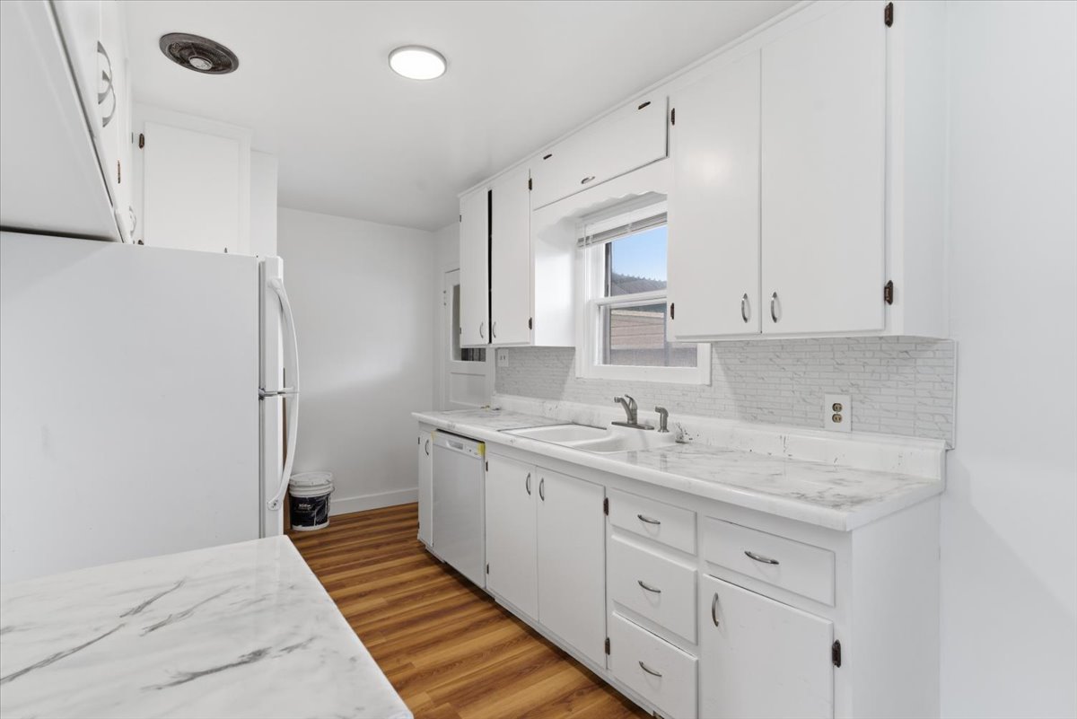 Kitchen featuring white appliances, light countertops, white cabinets, light wood finished floors, and backsplash