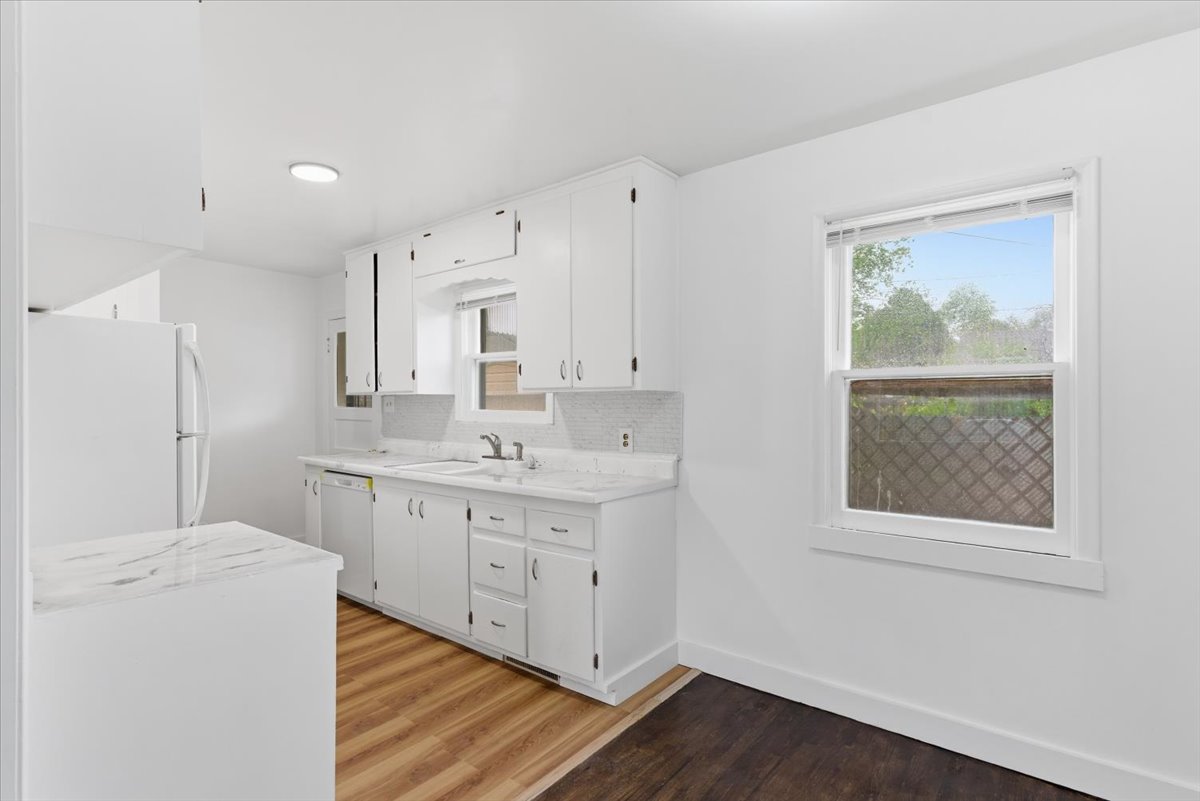 Kitchen featuring light countertops, light wood-type flooring, white appliances, white cabinetry, and tasteful backsplash