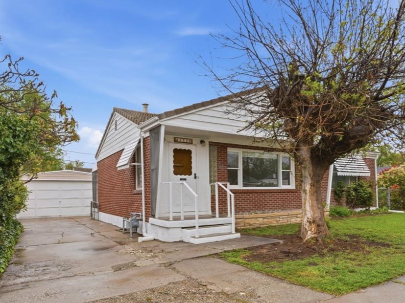 Bungalow-style home featuring an outbuilding, brick siding, a detached garage, and a front yard