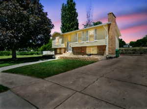 Split foyer home featuring a yard, brick siding, a chimney, and driveway