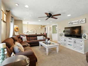 Living area with hanging lights, light carpet, a ceiling fan, and a textured ceiling