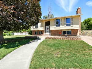 Split foyer home with a front yard, a chimney, and brick siding