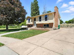 Raised ranch featuring a front lawn, a chimney, brick siding, and concrete driveway