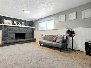 Living area with carpet floors, a brick fireplace, a textured ceiling, and a wainscoted wall
