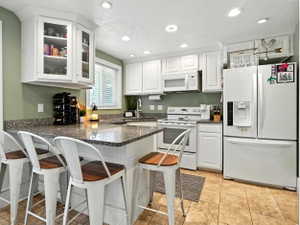 Kitchen featuring white appliances, a breakfast bar area, white cabinets, a peninsula, and dark stone countertops