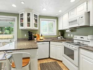 Kitchen with white appliances, a peninsula, white cabinets, a kitchen bar, and recessed lighting