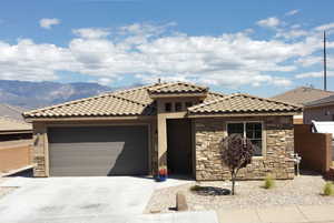View of front of home with stone siding, a garage, driveway, and a tile roof