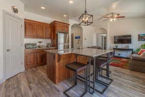 Kitchen featuring a kitchen bar, wood finish cabinetry, open floor plan, light stone countertops, and a center island with sink