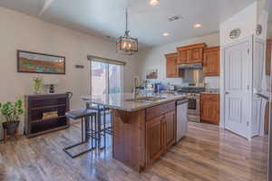Kitchen with wood finish cabinetry, light stone counters, stainless steel appliances, a kitchen island with sink