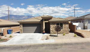Single story home featuring stone siding, concrete driveway, a garage, and a mountain view