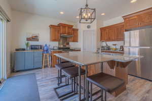 Kitchen with wood finish cabinets, stainless steel appliances, a kitchen island with sink, light stone counters, and a breakfast bar area