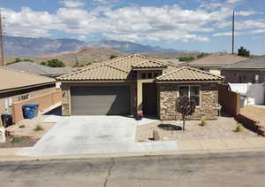 View of front of home with stone siding, a garage, concrete driveway, and a mountain view