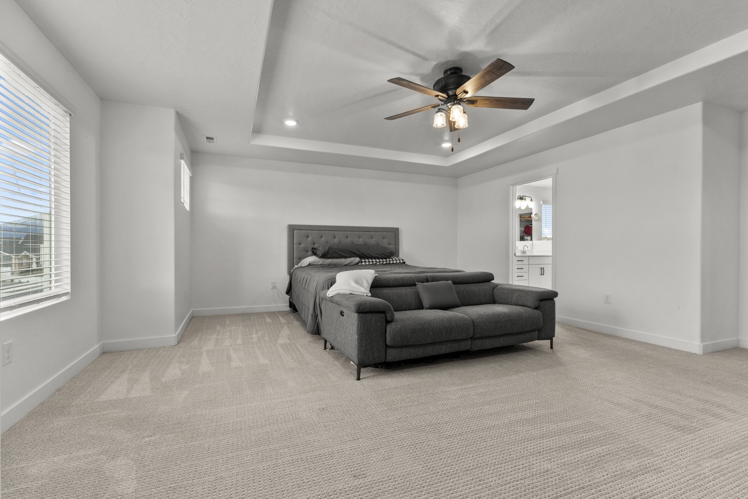 Bedroom with light colored carpet, a ceiling fan, a tray ceiling, and ensuite bathroom