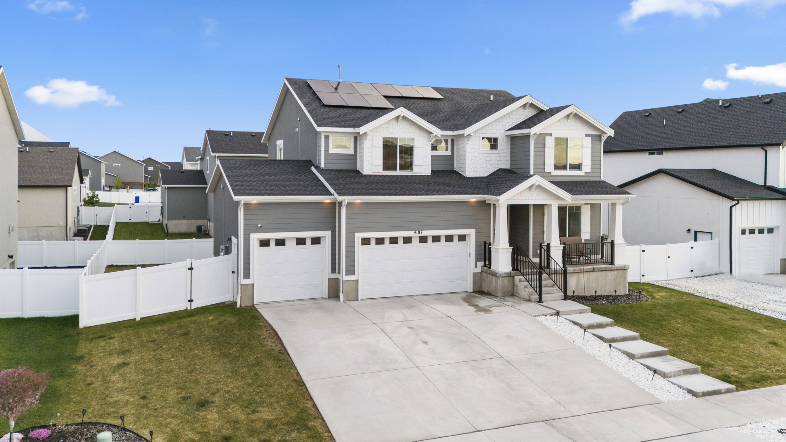 Modern farmhouse featuring a gate, solar panels, concrete driveway, and roof with shingles