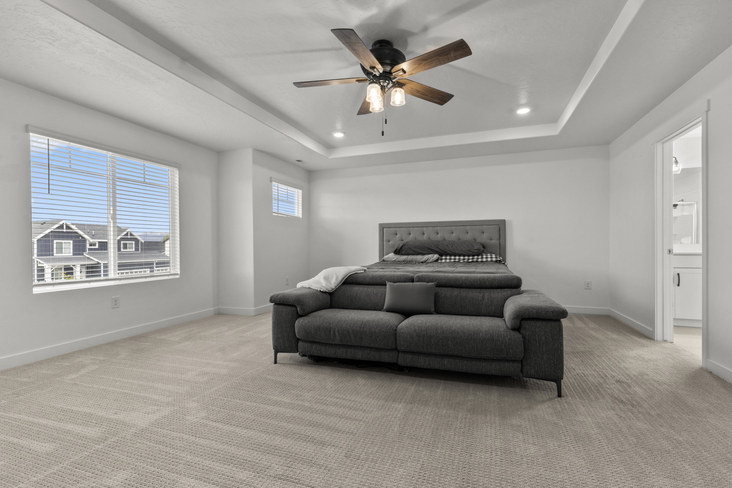 Bedroom with light colored carpet, a ceiling fan, and a raised ceiling