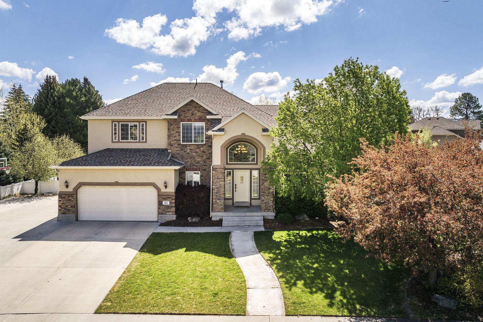 View of front facade with stucco siding, a front lawn, driveway, a garage, and stone siding