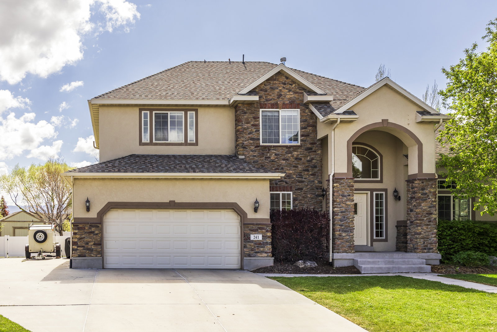 View of front of house with stone siding, driveway, stucco siding, and a garage