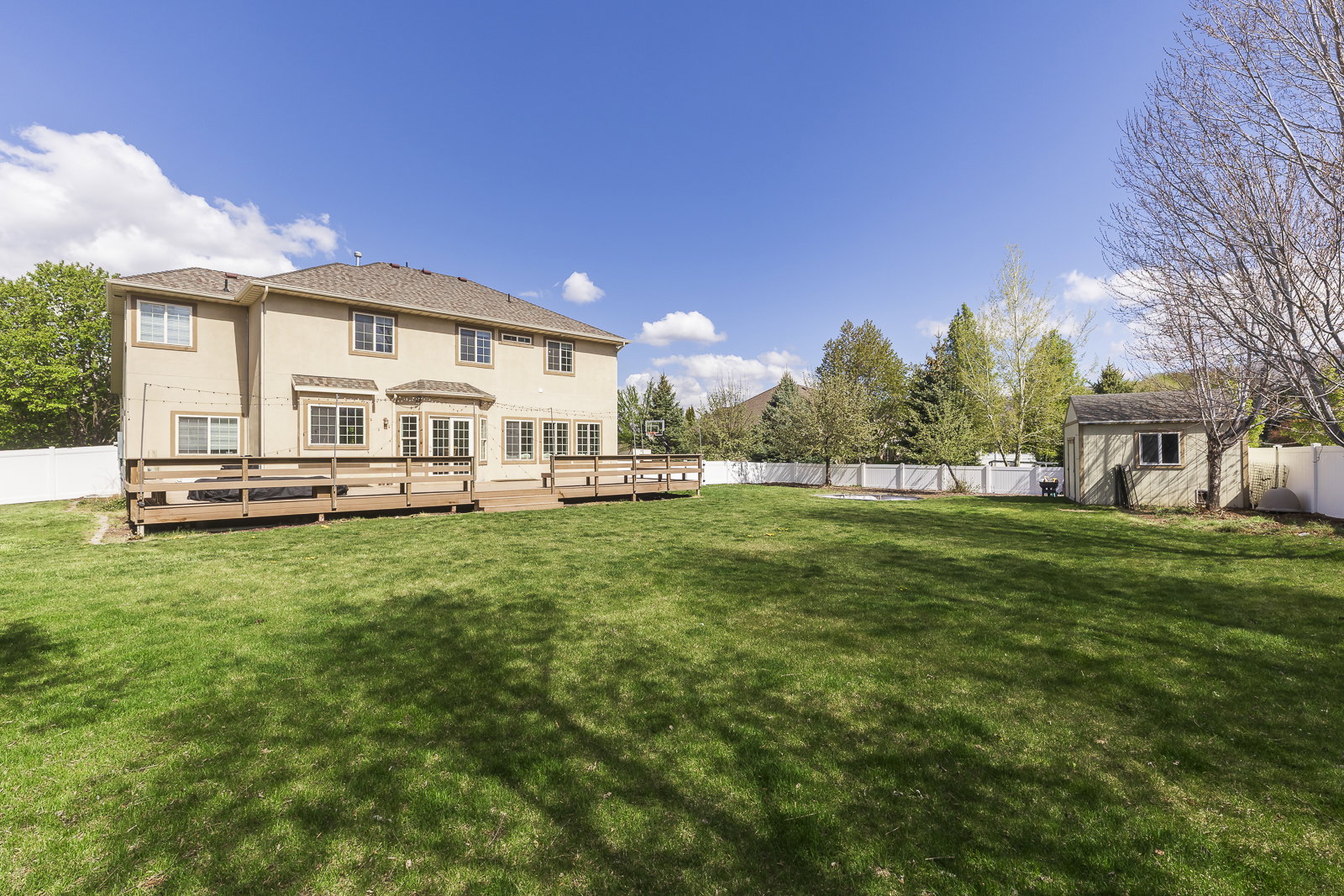 Back of house featuring a fenced backyard, a deck, stucco siding, and a storage shed