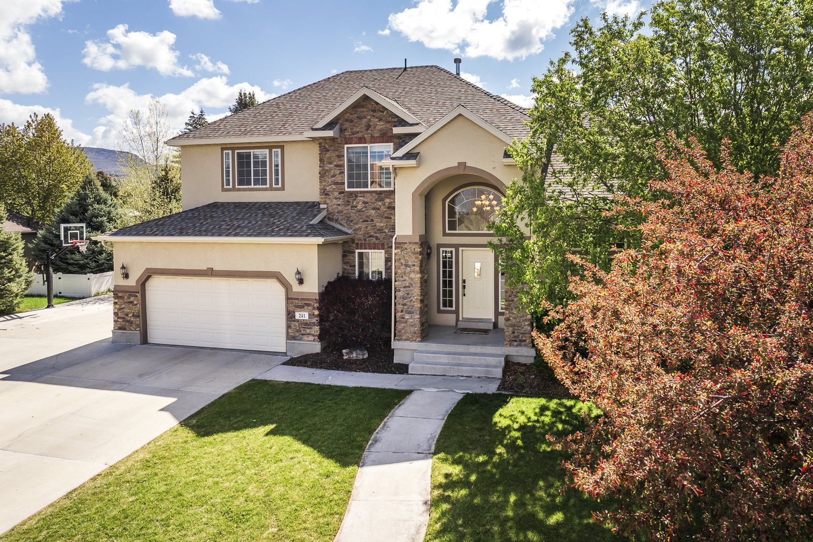 View of front facade with driveway, stone siding, stucco siding, and a garage