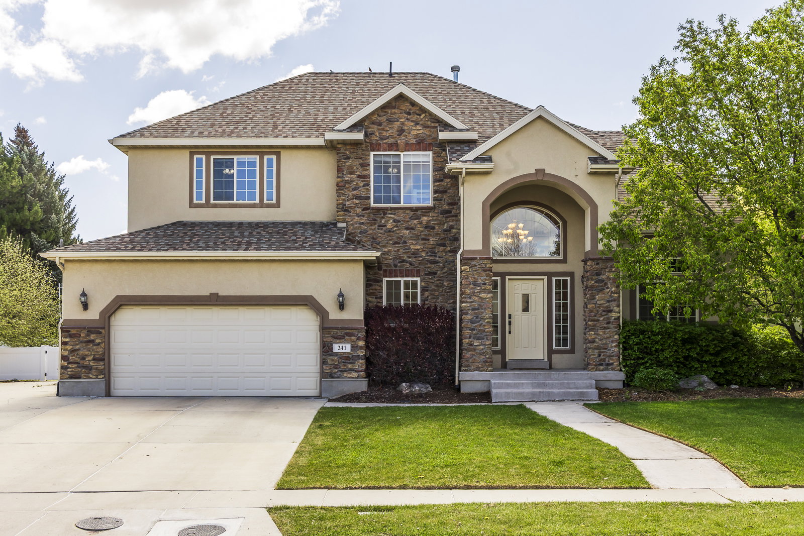 View of front of home featuring stucco siding, concrete driveway, stone siding, a garage, and a front lawn