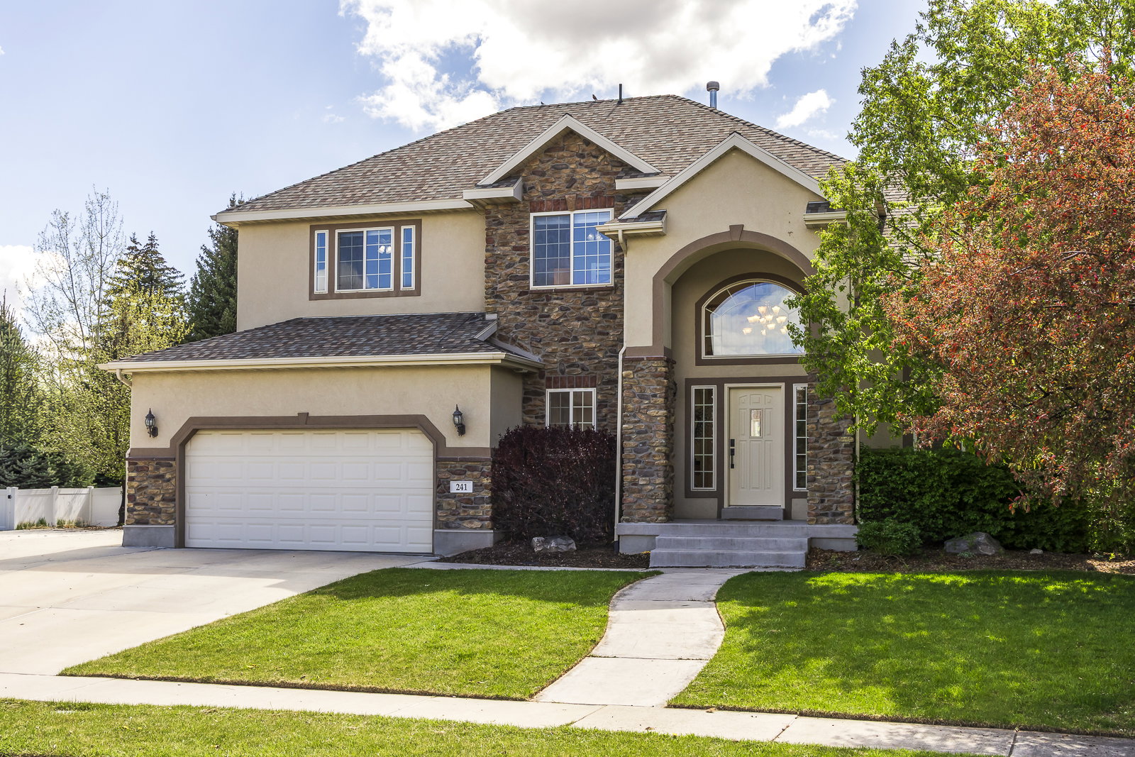 View of front of property with stucco siding, stone siding, driveway, and a front lawn
