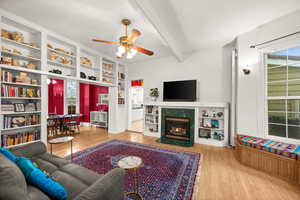 Main floor family room featuring gas fireplace, built in bookshelves,  light wood floors, ceiling fan, and bay window with bench