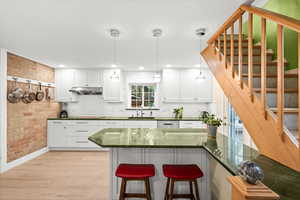 Kitchen with exposed brick wall, white cabinets, a breakfast bar, light wood-style floors and beautiful green granite counters