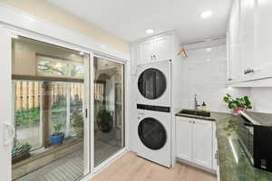 Newly remodeled laundry room with access to the greenhouse,  stacked washer / dryer, sink, storage cabinets, hanging bar, broom closet, shoe rack
