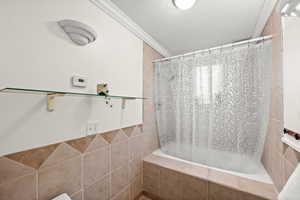 Bathroom featuring tiled shower / bath combo, crown molding, and tile walls