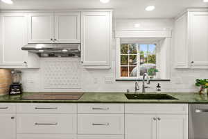Kitchen with white cabinets, stainless steel dishwasher, dark stone countertops, black electric cooktop, and recessed lighting